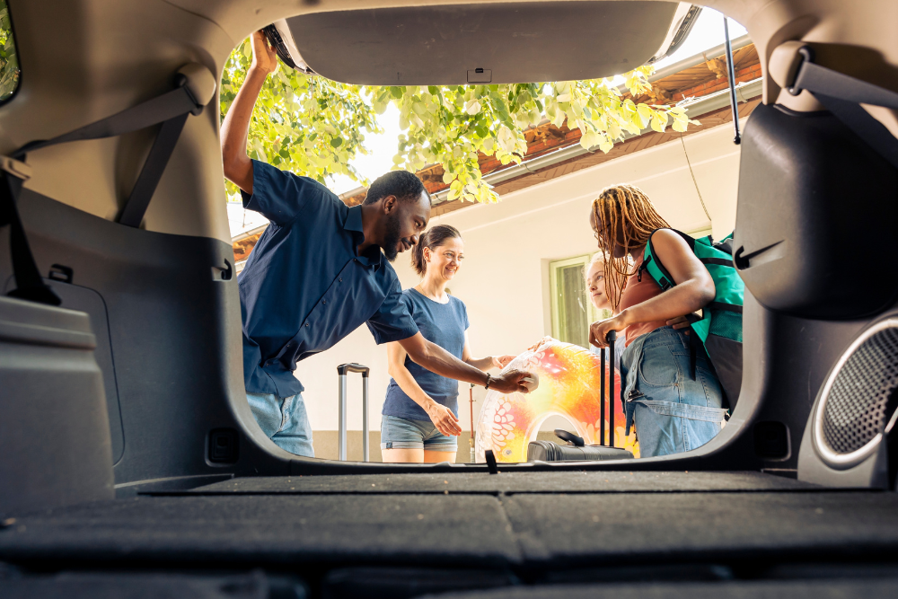 Car Checklist in Vacaville, CA at Motoring Specialists. View from inside an open car trunk as a group of people load luggage and a colorful inflatable into the vehicle, smiling and preparing for a trip.