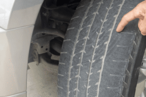 Uneven tire wear inspection by Motoring Specialists in Vacaville, CA. Image of a worn tire with a hand pointing to uneven tread wear, highlighting the need for tire and alignment service.